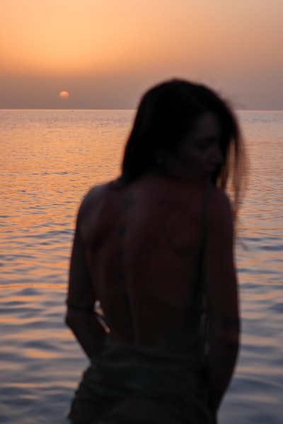 女人在棕色的外套站在海岸日落
